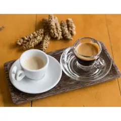 Dwie filiżanki kawy, jedna biała, druga szklana, obok garść ziaren kawy. To kawa z odchodów nietoperza, znana jako Kopi Luwak.