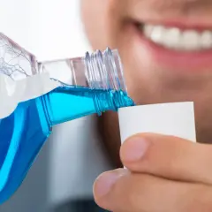 Un uomo versa colluttorio blu in un tappo, un gesto di cura dopo l'estrazione di un dente.