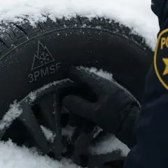 Policjant sprawdza oznaczenie 3PMSF na oponie w śniegu. Czy w Niemczech można jeździć na oponach wielosezonowych?