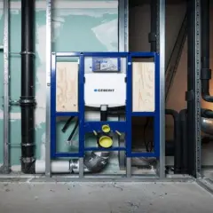 Montaż stelaża Geberit, widoczny podłączenie do odpływu. Instalacja hydrauliczna w trakcie budowy.