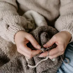 Dłonie tworzą ciepły sweter, pokazując różnicę między szydełkowaniem a robieniem na drutach.