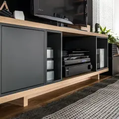 Nowoczesna szafka RTV z czarnymi frontami i drewnianymi elementami. W otwartych wnękach sprzęt audio-wideo, idealne miejsce, jak schować kable od telewizora.