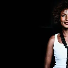 Waris Dirie w białej koszulce i czarnym naszyjniku, uśmiecha się.