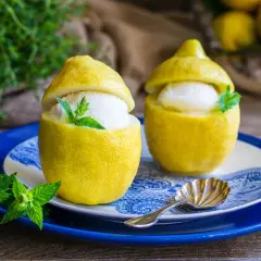 Delizioso gelato al limone servito in limoni svuotati, guarnito con menta fresca. Un'idea rinfrescante preparata con una gelatiera.