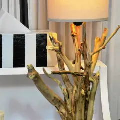 Oryginalna lampa z gałęzi, która wygląda jak małe drzewko, stoi obok ozdobnego pudełka na chusteczki.