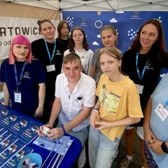Grupa osób, w tym młodzież i dorosłych, stoi za stołem z książkami i materiałami promocyjnymi "Szkoła w Chmurze".