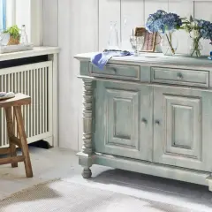 Ein blau-graues Sideboard mit abgenutzter Patina, das den "shabby chic"-Stil verkörpert. Daneben ein Holzhocker und Blumen.
