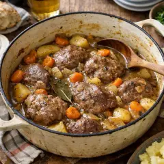 Un plat mijoté de joue de porc au cidre, avec des pommes de terre et des carottes, servi dans une cocotte en fonte.