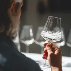 Un uomo assapora un bicchiere di vino bianco altoatesino, con altri calici sullo sfondo.