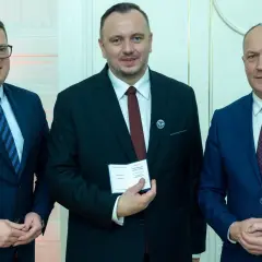 Trzech mężczyzn w garniturach. Środkowy, zasłużony dla kolejnictwa, trzyma certyfikat.