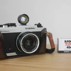 A silver and black Voigtlander Bessa-L camera in a brown leather case sits next to a box of Ilford XP2 Super 400 black and white film.