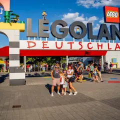 Rodzina pozuje przed wejściem do Lego Land Deutschland. Kolorowe klocki i wielkie logo zapraszają do świata zabawy.