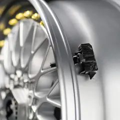 Czarny czujnik ciśnienia opon zamontowany na srebrnej feldze aluminiowej. Zbliżenie na element systemu monitorowania ciśnienia.
