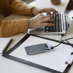 Un homme tape sur son ordinateur portable, un disque SSD externe est branché.