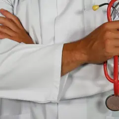 Lekarz w białym kitlu trzyma stetoskop. Jego ręce są skrzyżowane, co sugeruje spokój i doświadczenie w dziedzinie geriatrii.