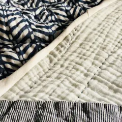 A close-up of a quilt shows a patterned blue fabric next to a textured white double gauze fabric, stitched with blue thread.