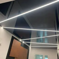 Nowoczesny sufit napinany w salonie z geometrycznymi wzorami i liniowym oświetleniem LED.