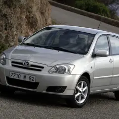 Srebrna Toyota Corolla E12 hatchback na krętej drodze wśród skał i zieleni.
