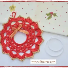 Ghirlanda natalizia uncinetto rossa con bordo dorato e fiocco, pronta per decorare.