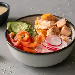 Kolorowa sałatka do sushi z łososiem, ryżem, ogórkiem, papryką i rzodkiewką. Obok miseczka z sosem.