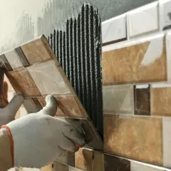 Pose de carrelage sur carrelage, une main gantée appliquant une nouvelle rangée sur le mur déjà carrelé.