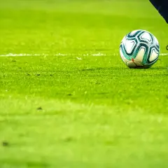 Piłkarz w butach piłkarskich i piłka na zielonej murawie.
