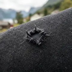 Ett hål i en svart dunjacka, redo för en lagningslapp. I bakgrunden syns norska fjordar och hus.