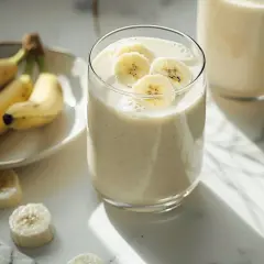 Pyszny koktajl bananowy, ozdobiony plasterkami banana, obok świeżych owoców na talerzyku. Idealny na orzeźwiający początek dnia.