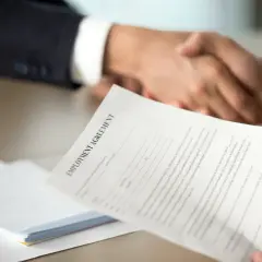 Poignée de main après la signature d'un contrat. Une lettre de motivation pour un poste d'assistant manager est visible.