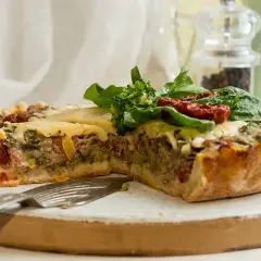 Pyszna tarta z mięsem mielonym, brokułami i suszonymi pomidorami, udekorowana świeżym szpinakiem.