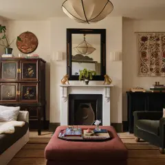 A living room with a plush ottoman, antique cabinet, and fireplace, showcasing a curated collection of minimalist home decor.