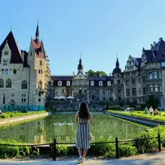 Zamek Moszna, gdzie jest? Piękny zamek z wieżami i stawem, z kobietą w pasiastej sukience patrzącą na niego.