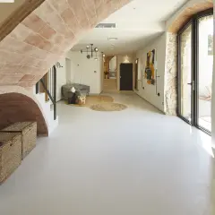 Nowoczesny hol z łukiem z cegły, gdzie **mikrocement na płytki** tworzy gładką, jednolitą podłogę. Wnętrze zdobią plecione kosze i abstrakcyjne obrazy.