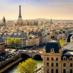 Vue panoramique de Paris en mars, avec la Tour Eiffel dominant un ciel clair. Les toits gris et les bâtiments haussmanniens s'étendent à perte de vue.