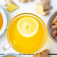 Tazza di bevanda gialla con limone, curcuma in polvere e radici, un potente antinfiammatorio naturale per intestino.