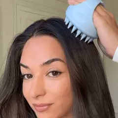 Mujer se masajea el cuero cabelludo con un cepillo azul para evitar cuando se cae mas el pelo.