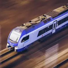 Białystok elk pędzi po torach. Nowoczesny pociąg Stadler PKP Intercity z niebiesko-białymi pasami mknie przez krajobraz.