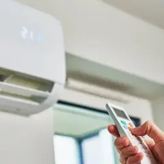 Mano ajustando el aire acondicionado con el control remoto. El símbolo del árbol en el control indica modo ecológico.