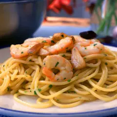 Espaguetis con gambas salteadas con ajo y perejil, servidos en un plato blanco con borde azul.