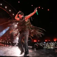 Manuel Carrasco, con un atuendo de flecos, canta enérgico en su gira. El público, con móviles en alto, graba el momento.