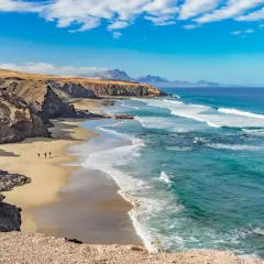 Plaża na Fuerteventurze, idealne miejsce, by poczuć, kiedy najlepiej na Kanary. Surferzy idą w stronę oceanu.