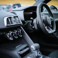 Interno di un'auto sportiva con volante a sinistra. Il cruscotto è scuro, con bocchette d'aria cromate e un display digitale. La leva del cambio è in primo piano. Perfetta per esplorare paesi con guida a sinistra.