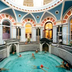 Wnętrze z basenem, gdzie ludzie relaksują się w gorącym źródle. Architektura jest bogato zdobiona, z niebieskimi i pomarańczowymi detalami.