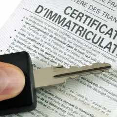 Une main tient une clé de voiture au-dessus d'un certificat d'immatriculation français. C'est le document essentiel pour type mine carte grise.