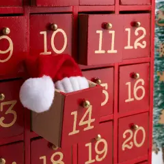 Un calendario dell'Avvento rosso con cassetti numerati. Il cassetto 11 è aperto, mostrando un cappellino di Babbo Natale. Ideale per idee su cosa mettere nel calendario avvento.