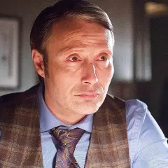 Mads Mikkelsen i en Mads Mikkelsen serie, klädd i skjorta, väst och slips. En annan person syns suddigt i bakgrunden.