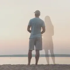 Uomo in piedi sulla spiaggia, con la figura evanescente di una donna accanto. Un'immagine che evoca il sentirsi soli in coppia.
