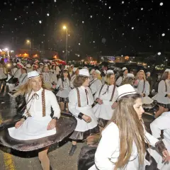 Desfile de mujeres con trajes blancos y sombreros en el carnaval cabezon de la sal, bajo una noche lluviosa.