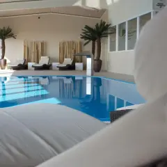Relaks przy basenie w hotelu Radisson Blu Cottbus. Leżaki czekają na gości obok błękitnej wody i palm.