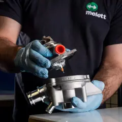Mano con guante azul sostiene un turbo y su carcasa, inspeccionando posible perdida de aceite por el turbo.